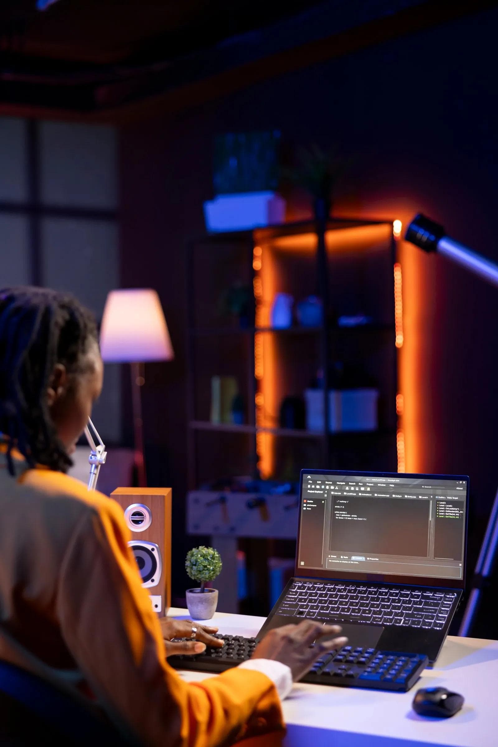 Developer working in a code editor on a laptop in a dark room lit by orange strip lighting.